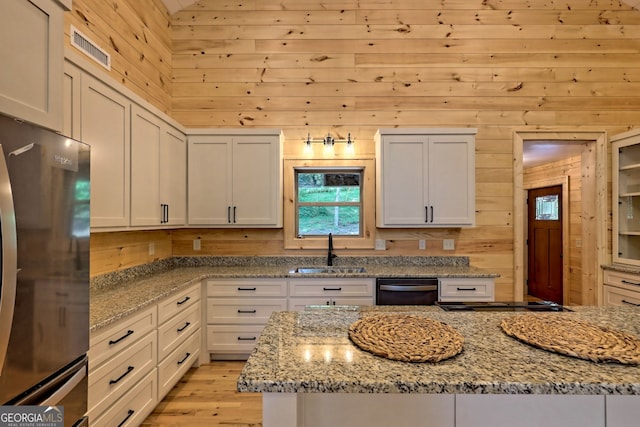 kitchen featuring sink, white cabinetry, stainless steel refrigerator, dishwasher, and light stone countertops