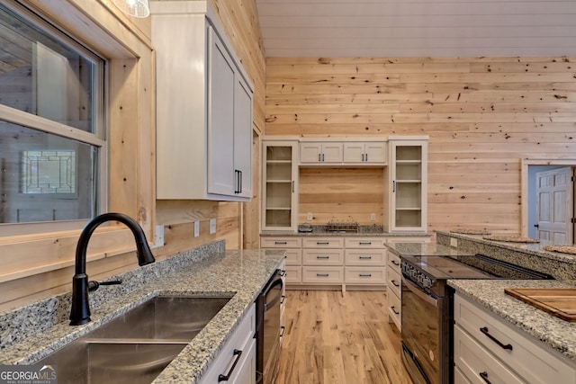 kitchen featuring sink, light stone counters, black appliances, wooden walls, and white cabinets