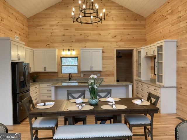 dining room featuring light wood-type flooring, high vaulted ceiling, wooden walls, and sink