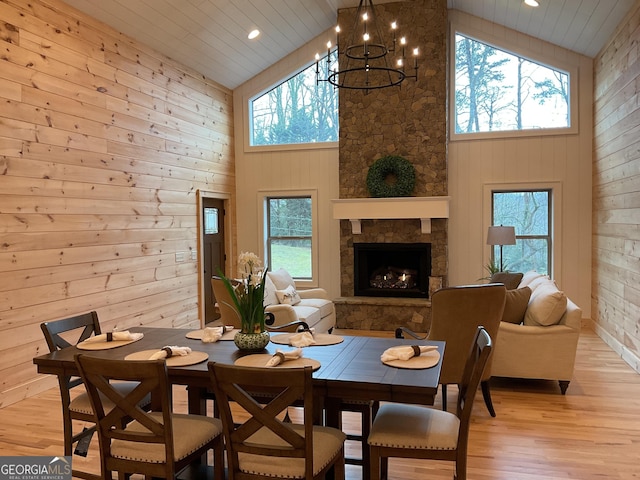 dining space with light hardwood / wood-style flooring, a stone fireplace, a wealth of natural light, and wooden walls