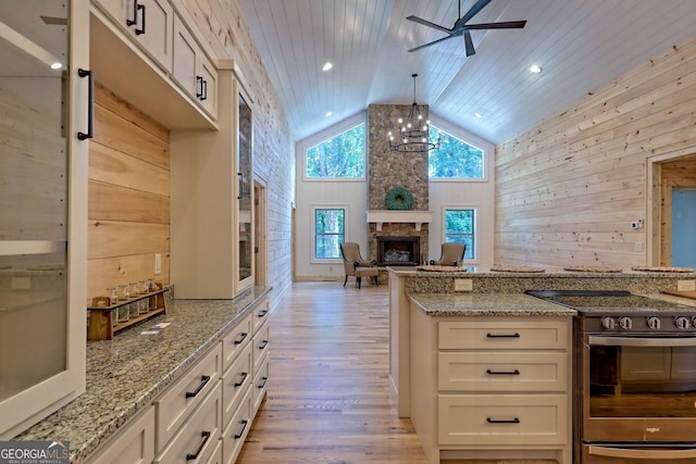 kitchen with a fireplace, wood walls, decorative light fixtures, stainless steel range with electric cooktop, and light stone counters