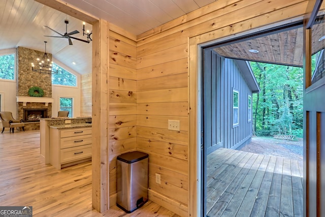 doorway to outside featuring lofted ceiling, light hardwood / wood-style flooring, a stone fireplace, wooden walls, and a chandelier