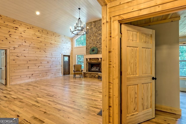 interior space featuring a fireplace, wooden walls, an inviting chandelier, and light hardwood / wood-style flooring