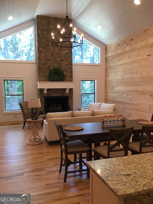 dining room featuring hardwood / wood-style flooring, wooden walls, a stone fireplace, and a wealth of natural light