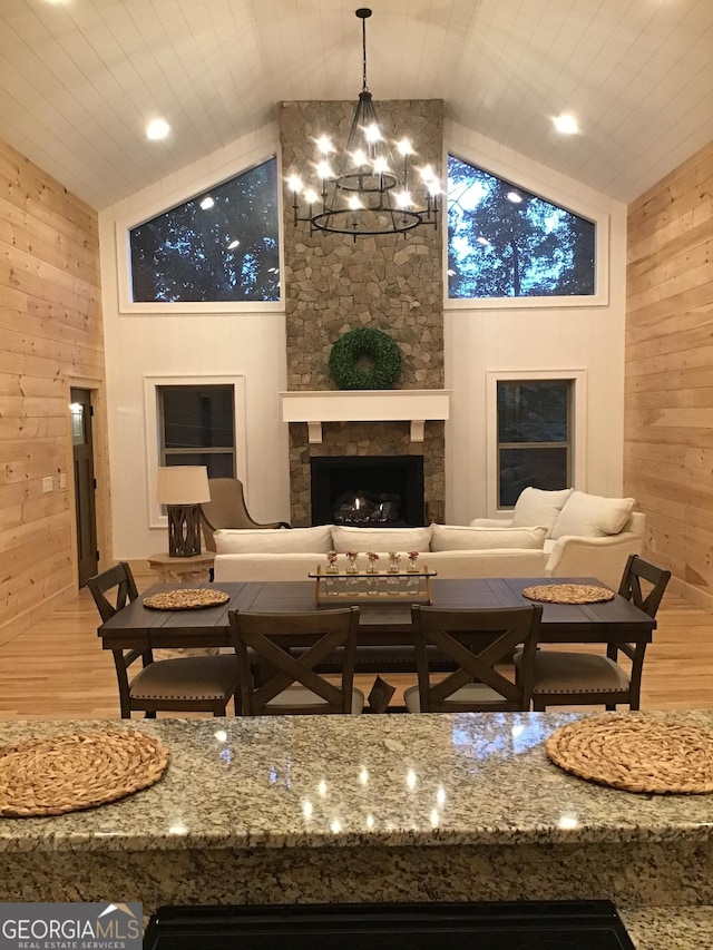 interior space featuring lofted ceiling, an inviting chandelier, wood-type flooring, wooden walls, and a fireplace