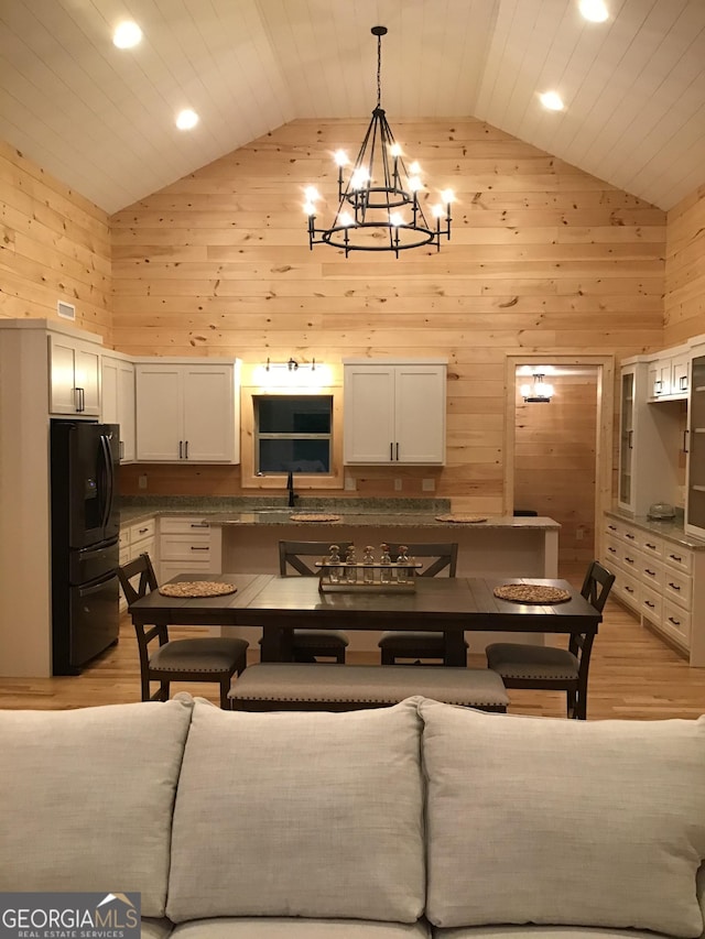 kitchen with white cabinetry, black refrigerator with ice dispenser, high vaulted ceiling, and wooden walls