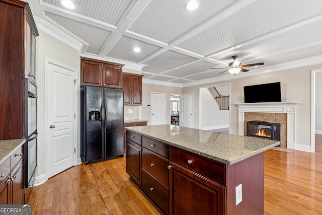 kitchen with coffered ceiling, light wood-type flooring, a kitchen island, light stone countertops, and black appliances