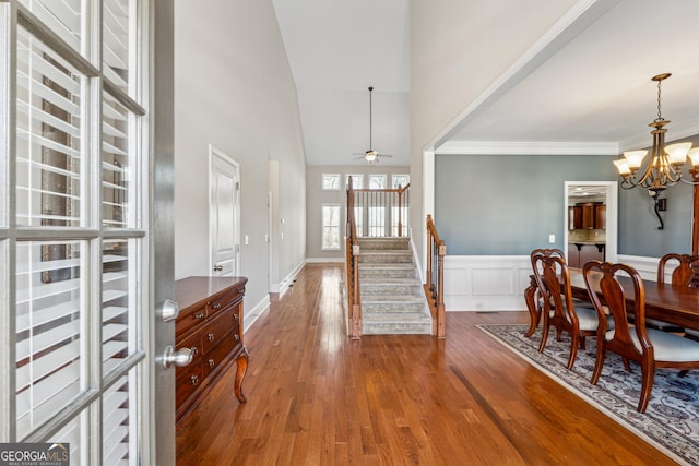 foyer entrance with hardwood / wood-style flooring, crown molding, a towering ceiling, and ceiling fan with notable chandelier