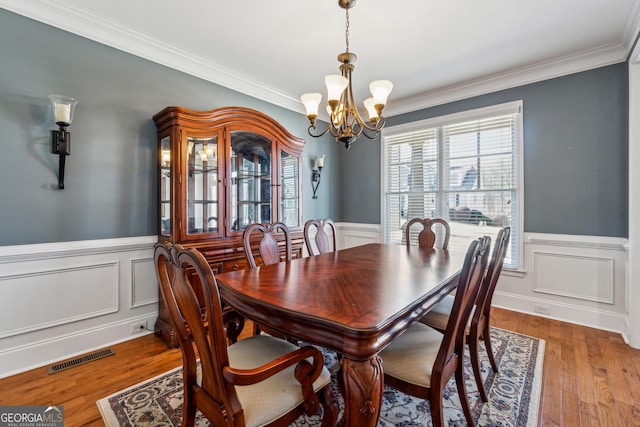 dining space with ornamental molding, hardwood / wood-style floors, and a notable chandelier