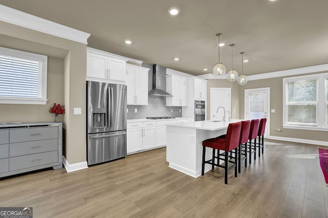 kitchen with wall chimney exhaust hood, appliances with stainless steel finishes, a center island with sink, and white cabinets