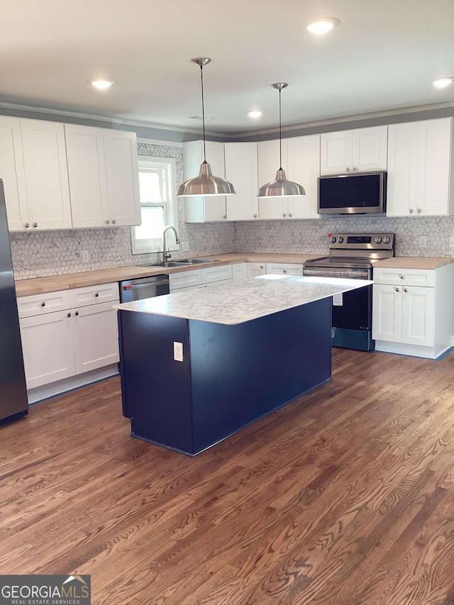 kitchen with sink, a kitchen island, pendant lighting, stainless steel appliances, and white cabinets