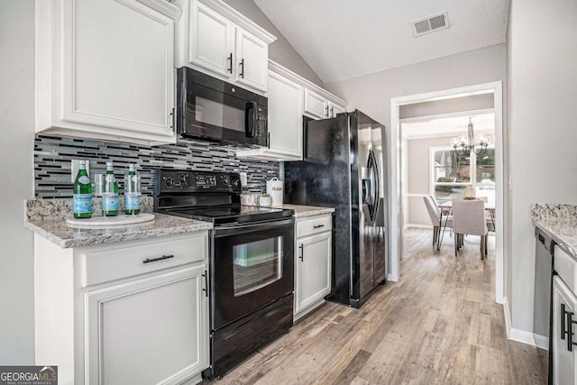 kitchen featuring lofted ceiling, white cabinetry, light stone counters, black appliances, and decorative backsplash