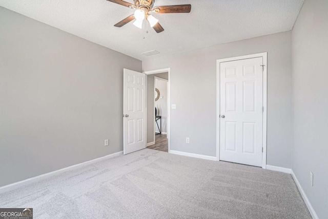 unfurnished bedroom with ceiling fan, light colored carpet, and a textured ceiling