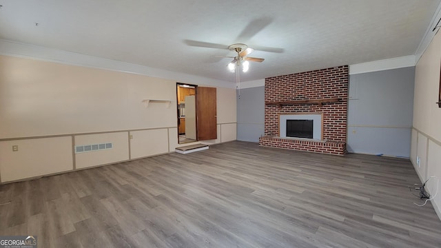 unfurnished living room with a textured ceiling, light wood-type flooring, ornamental molding, ceiling fan, and a fireplace