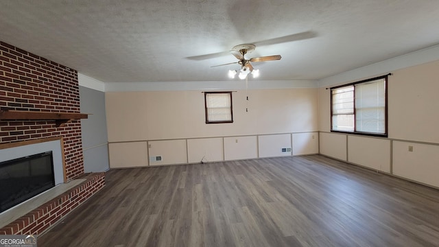 unfurnished living room with ceiling fan, a fireplace, dark hardwood / wood-style floors, and a textured ceiling