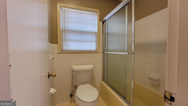 bathroom with enclosed tub / shower combo, tile walls, and toilet