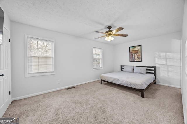 bedroom with ceiling fan, light carpet, and a textured ceiling