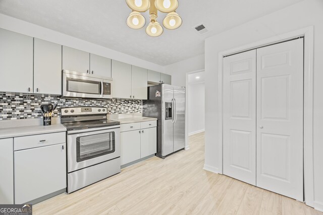 kitchen with tasteful backsplash, appliances with stainless steel finishes, an inviting chandelier, and light hardwood / wood-style flooring