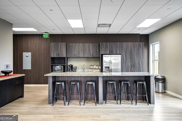 kitchen with a breakfast bar area, a kitchen island with sink, stainless steel refrigerator with ice dispenser, light stone counters, and light hardwood / wood-style floors