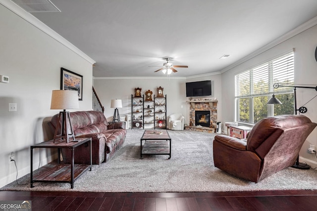 living room with hardwood / wood-style flooring, ornamental molding, a stone fireplace, and ceiling fan