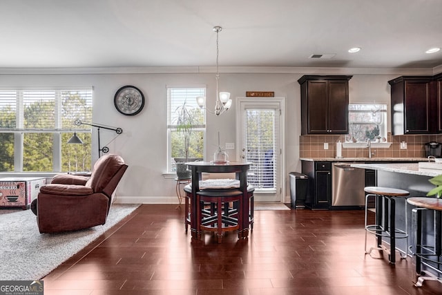 kitchen featuring dishwasher, decorative backsplash, hanging light fixtures, dark brown cabinetry, and light stone countertops