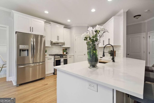 kitchen featuring appliances with stainless steel finishes, white cabinets, a kitchen breakfast bar, ornamental molding, and kitchen peninsula