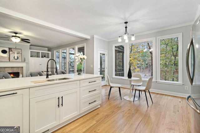 kitchen with sink, stainless steel refrigerator, pendant lighting, a tiled fireplace, and white cabinets