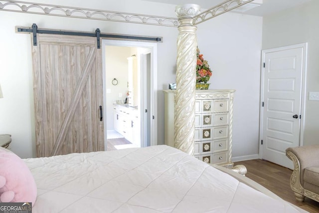 bedroom with ensuite bathroom, a barn door, and hardwood / wood-style floors