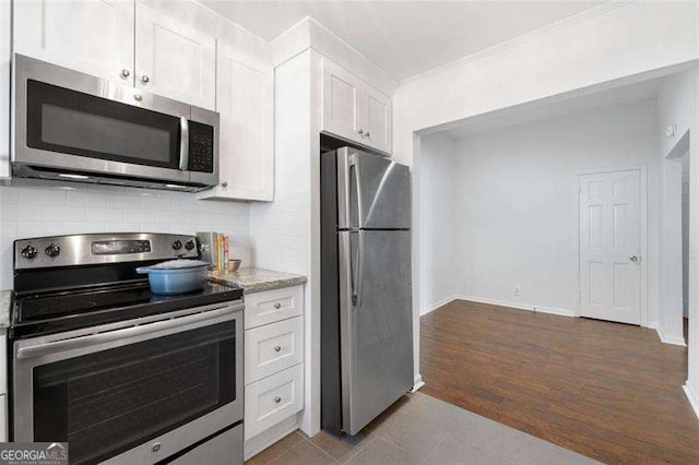 kitchen with white cabinetry, light stone counters, appliances with stainless steel finishes, hardwood / wood-style flooring, and backsplash