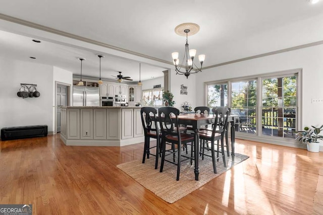 dining space with crown molding, ceiling fan with notable chandelier, a wealth of natural light, and light hardwood / wood-style flooring