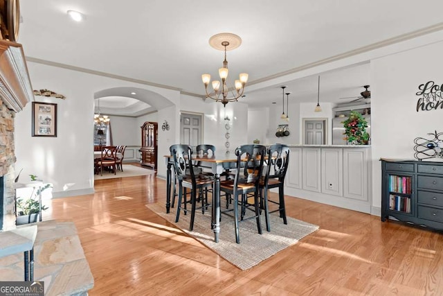 dining room with ceiling fan with notable chandelier, ornamental molding, a tray ceiling, and light hardwood / wood-style floors