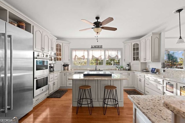 kitchen with a kitchen island, stainless steel appliances, white cabinets, a kitchen bar, and decorative light fixtures