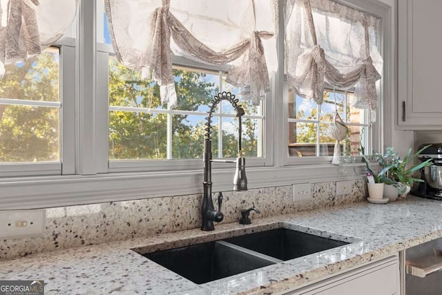 interior details with white cabinetry, sink, and light stone countertops