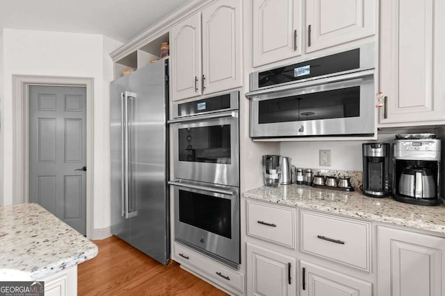 kitchen featuring white cabinetry, light stone countertops, stainless steel appliances, and light hardwood / wood-style floors