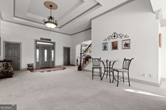 carpeted foyer featuring crown molding, a towering ceiling, and a tray ceiling