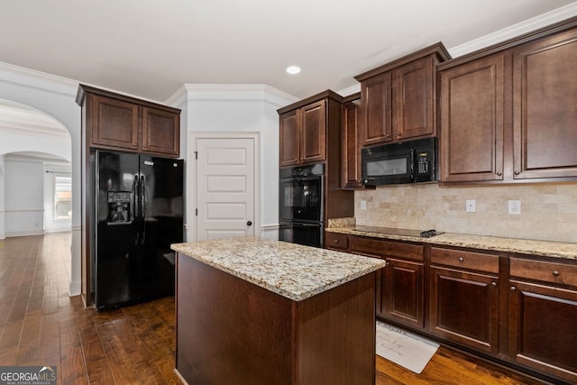 kitchen featuring backsplash, light stone counters, dark brown cabinetry, black appliances, and a kitchen island