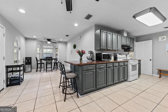 kitchen featuring light tile patterned flooring, a breakfast bar, white electric range, gray cabinetry, and ceiling fan