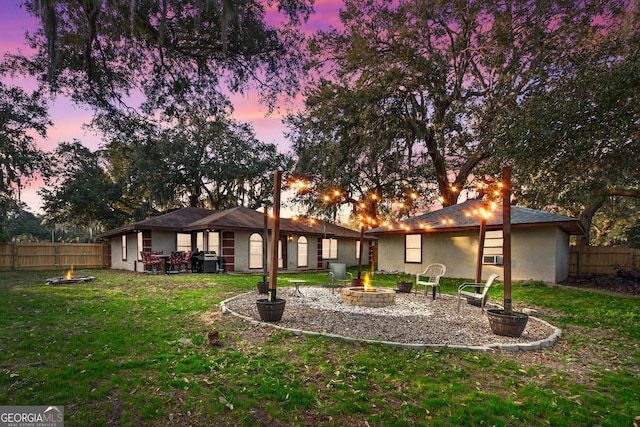 back house at dusk featuring a lawn and a fire pit