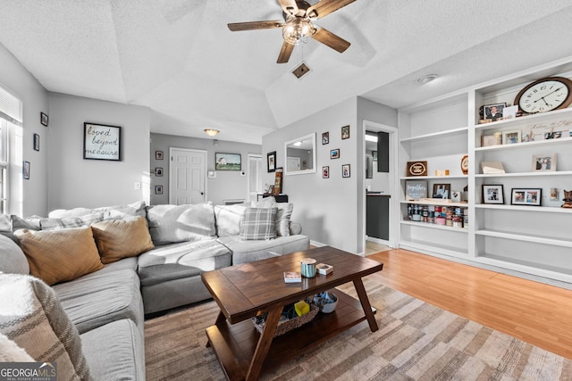 living room with lofted ceiling, ceiling fan, wood-type flooring, a textured ceiling, and built in shelves