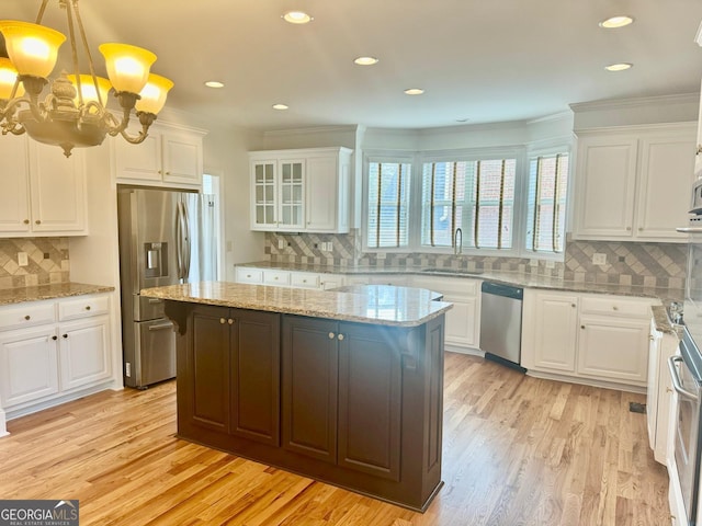 kitchen featuring sink, appliances with stainless steel finishes, a kitchen island, pendant lighting, and white cabinets