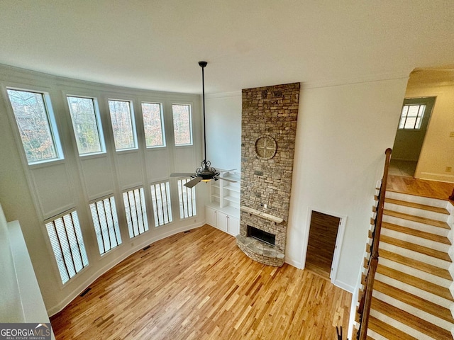 living room featuring built in shelves, a stone fireplace, ceiling fan, and light hardwood / wood-style flooring