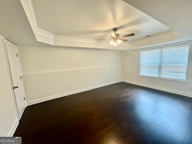 unfurnished room with a tray ceiling, dark wood-type flooring, and ornamental molding