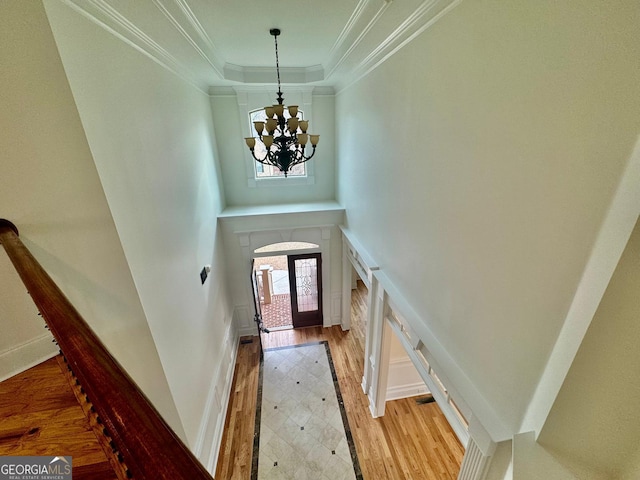 foyer entrance with ornamental molding, a raised ceiling, a chandelier, and light wood-type flooring