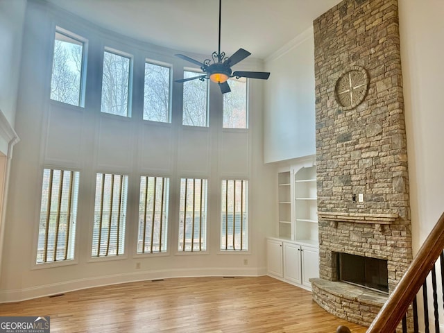 unfurnished living room featuring a fireplace, a high ceiling, ornamental molding, ceiling fan, and light hardwood / wood-style floors