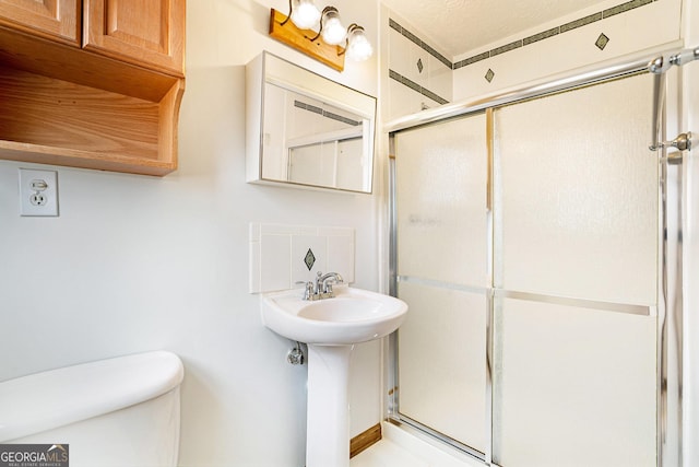 bathroom featuring toilet, a shower with shower door, and sink