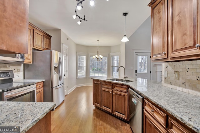 kitchen featuring stainless steel appliances, decorative light fixtures, light stone countertops, and sink