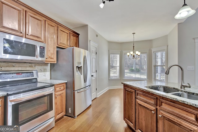 kitchen with stainless steel appliances, light stone countertops, sink, and pendant lighting