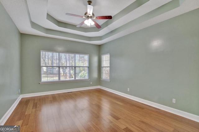 unfurnished room featuring a raised ceiling, wood-type flooring, and ceiling fan