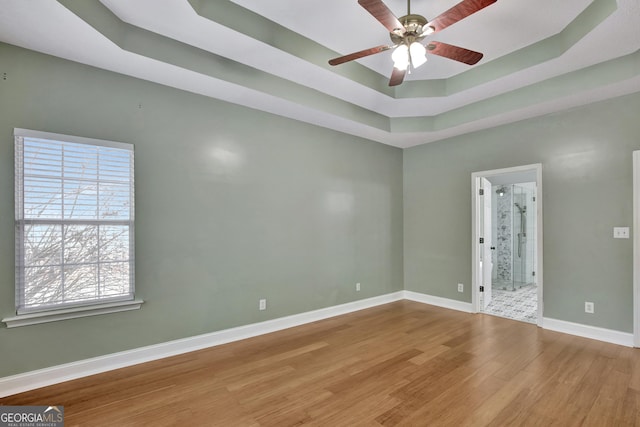 unfurnished room featuring ceiling fan, wood-type flooring, and a tray ceiling