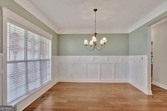 unfurnished dining area featuring ornamental molding, a notable chandelier, and light hardwood / wood-style flooring